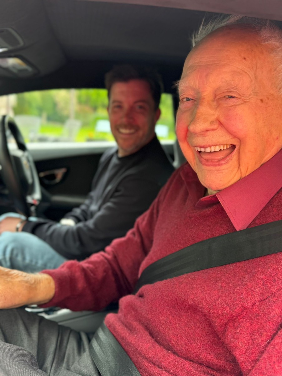 Two people laughing in the front seats of a Granborghini car, one at the wheel